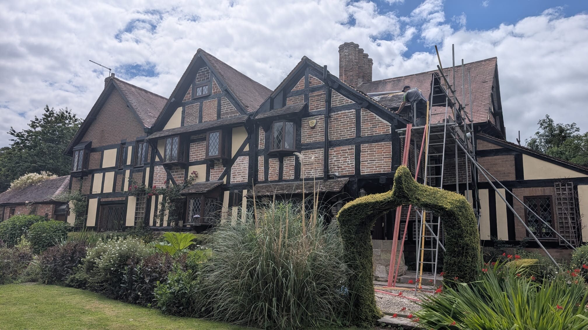 Roofer working on the handmade clay tile roof of the listed Barnt Green property from scaffold and ladder access